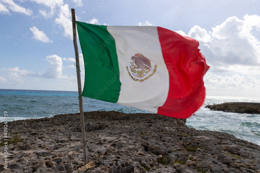 National flag of Mexico blows in the wind on a limestone beach on the tropical island of Cozumel.