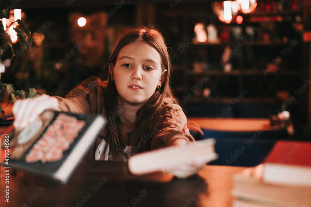 A cute teenage girl reading book in cafe. Education, leisure, hobby, back to school concept.