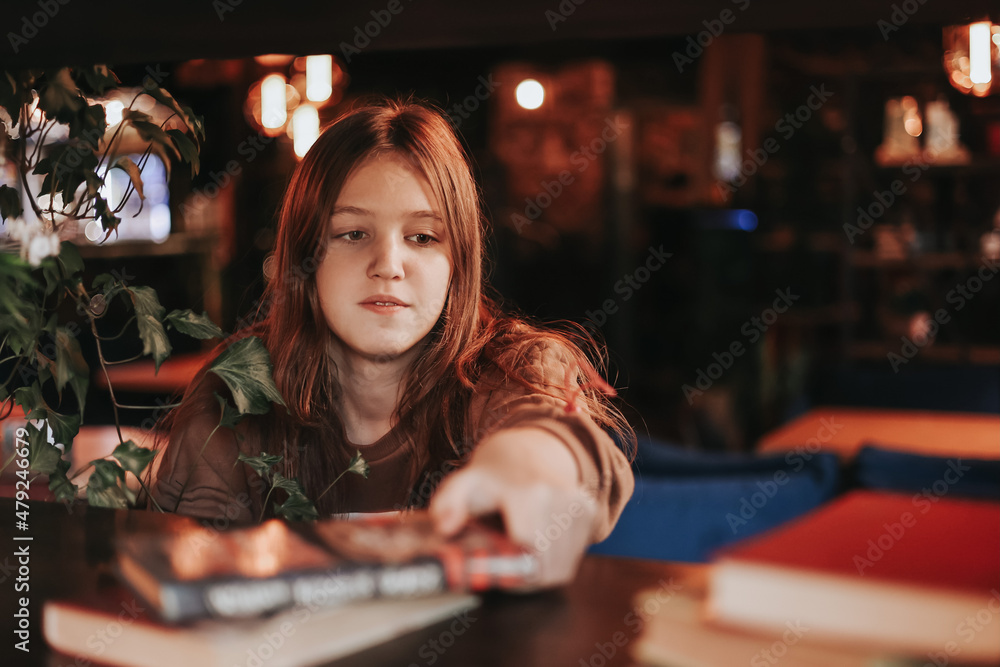 Fototapeta premium A cute teenage girl reading book in cafe. Education, leisure, hobby, back to school concept.