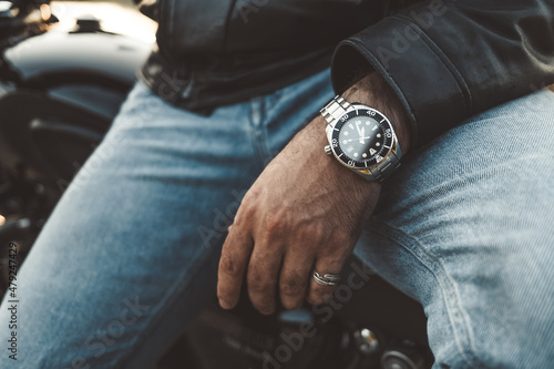 Male wrists, expensive watch close-up. Hands of young man sitting on motorcycle. Concept of luxury life, clock, punctuality, time