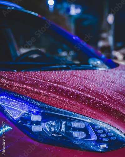 Rain drops on red car. Neon street lights reflecting on the car's surface. Stunning night photography. High quality photo