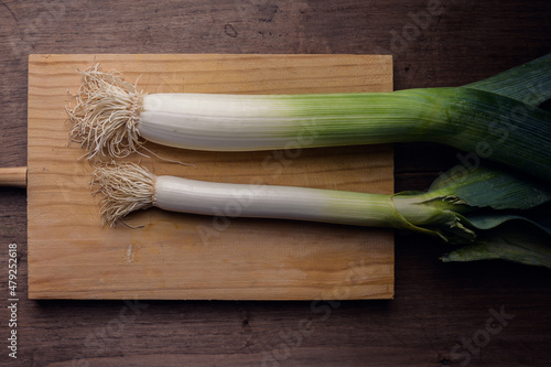 A leek resting on a wooden chopping board on a rustic wooden table in a dark environment.
