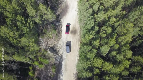 Two minivans, red and silver, are driving along a forest road. View from above. shooting from a drone, the camera moves to the right.