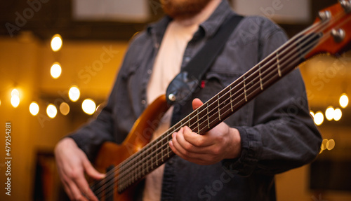 A young guy with a beard plays a bass guitar with five strings