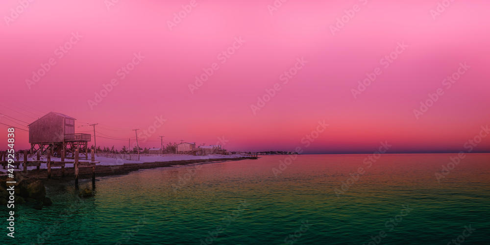 Foggy pink sunset along the coastal beach road with turquoise-colored seawater Bay. Saturated vibrant seascape with space for texts and design.