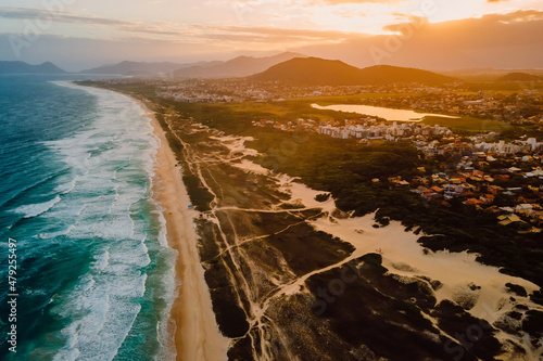 Sandy beach with dunes, ocean and town with sunset in Campeche, Florianopolis photo