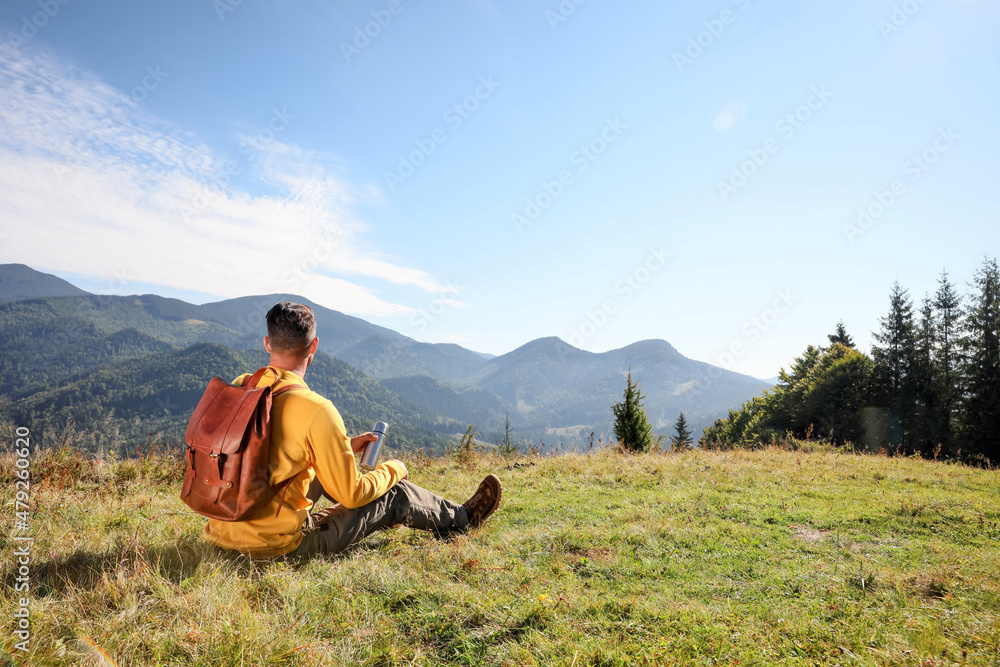 Tourist with thermos and backpack enjoying beautiful mountain landscape, back view.