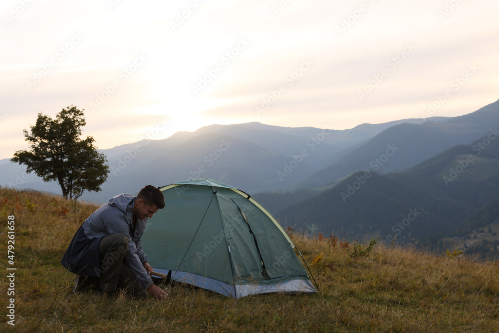 Man setting up camping tent in mountains at sunset