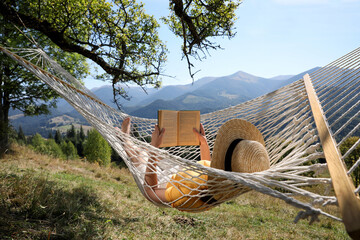 Young woman reading book in hammock outdoors on sunny day