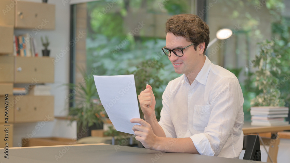 Young Man Feeling Happy while Reading Documents in Modern Office Young Man Feeling Happy while Reading Documents in Modern Office