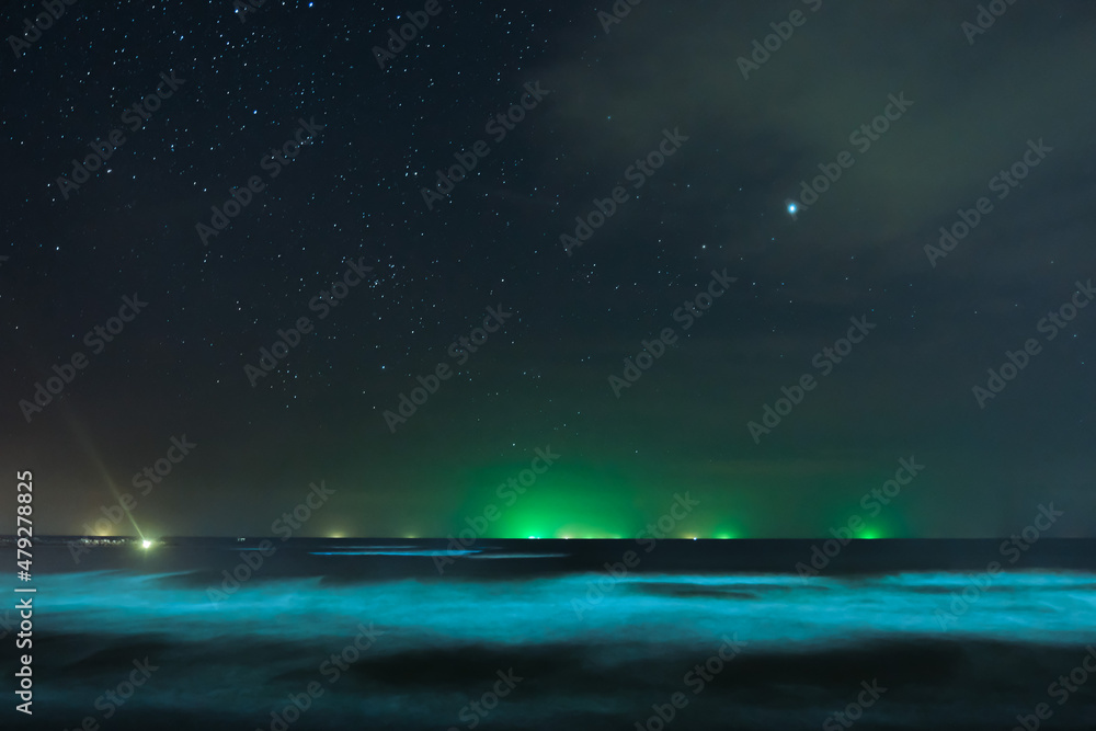 Stars in the night sky and green lights from a fishing boat at sea.