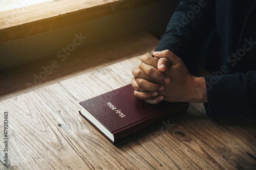 Handsome man hands are praying for God's blessings on bible with window light Pray in the Morning. begging for forgiveness and believing in goodness.