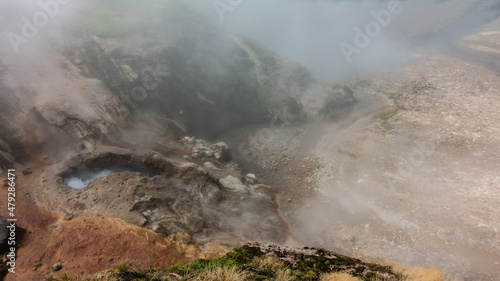 Geyser cauldron on the hillside. Boiling water foams. Hot steam hides the surroundings. A river flows through a rocky bed from thermal springs. Kamchatka. Valley of Geysers