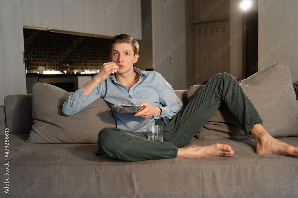 Relaxed European man spending his free time at home eating food and watching TV. caucasian guy enjoying movie relaxing on sofa in living room interior