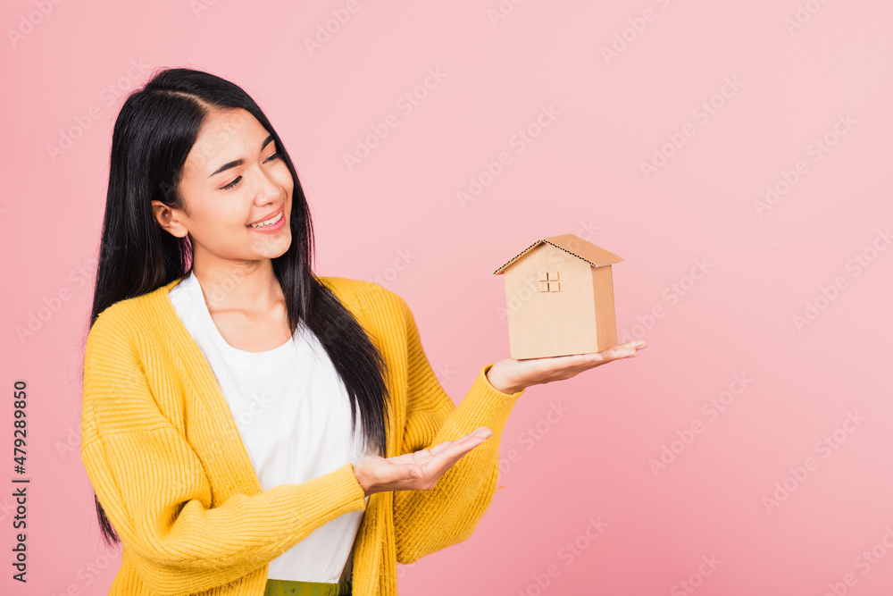 Happy Asian portrait beautiful cute young woman excited smiling holding house model on hand, studio shot isolated on pink background, broker female hold home real estate insurance and banking concept