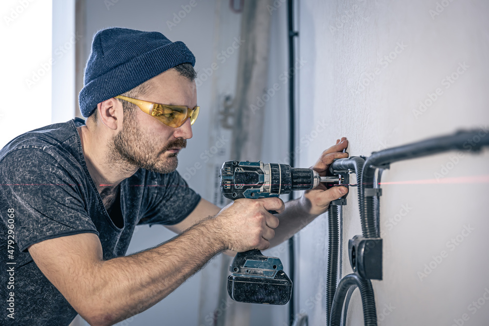 An electrician is mounting electric sockets on the white wall indoors. An electrician is mounting electric sockets on the white wall indoors.