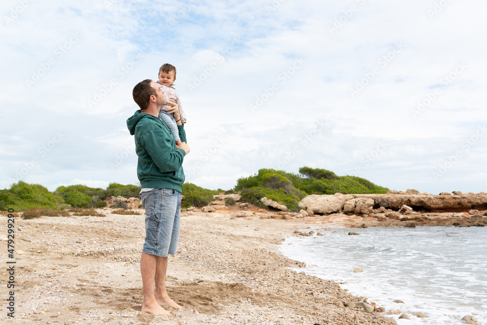 Standing man holding his little girl while looking at each other and smiling. Father and daughter having fun at the beach. Love and fatherhood. 