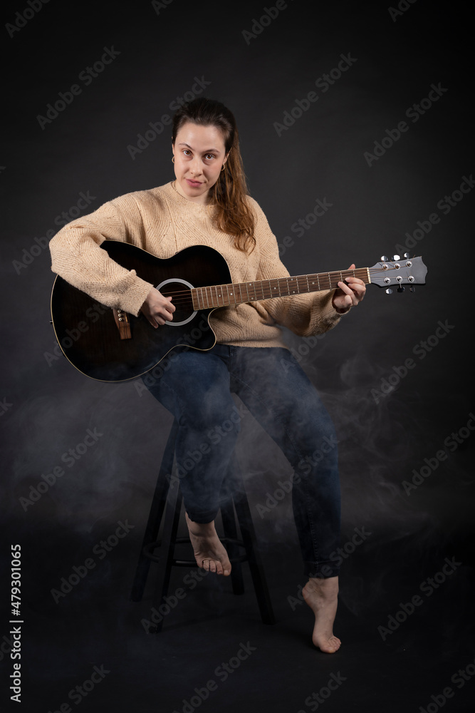 Young woman playing acoustic guitar with smoke and black background