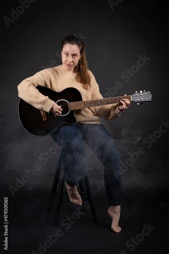 Young woman playing acoustic guitar with smoke and black background