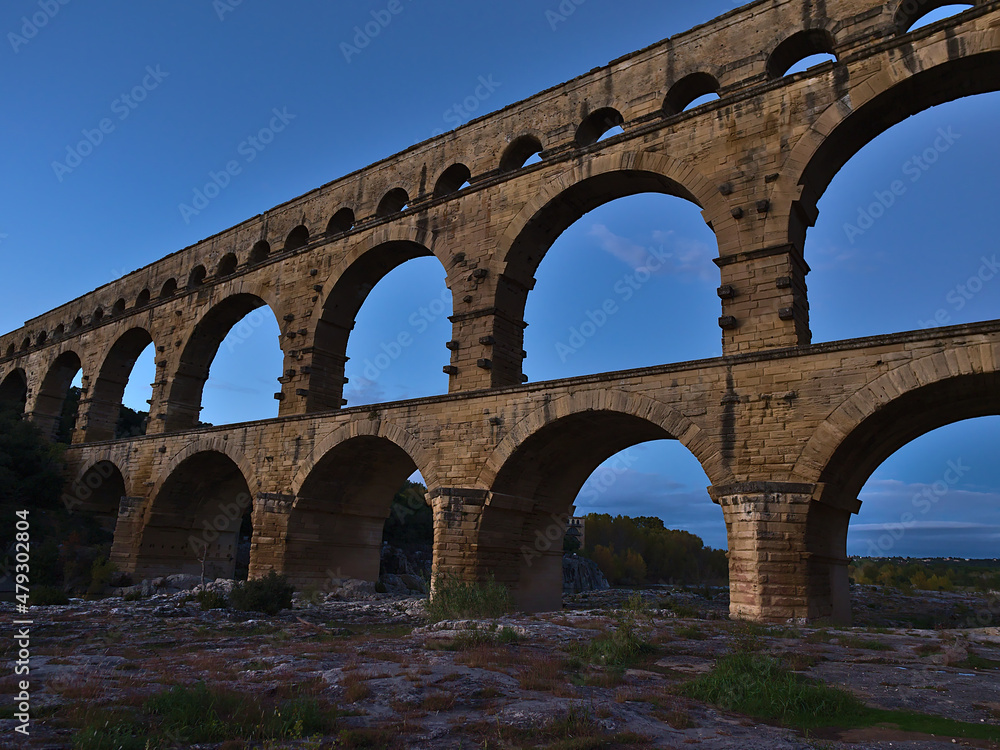 Beautiful view of ancient Roman aqueduct Pont du Gard with stone arches crossing Gardon river in the evening near Vers-Pont-du-Gard, Occitanie, France.