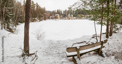 Wooden bench by the frozen blue lake. Winter tracking in popular in Adrspach rocks