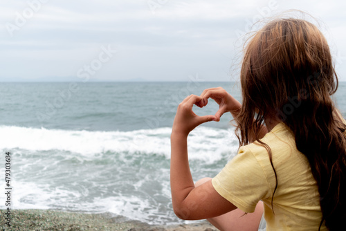 Child girl sits on the stones, hugging her knees. Adventure by the sea.