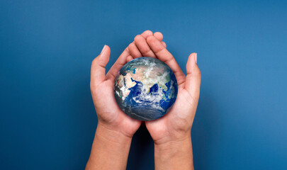 Earth in hands. World, small globe hold and supported by human hand with love and care, on blue background. Earth day. Save the planet. Energy saving concept. Elements of this image furnished by NASA.