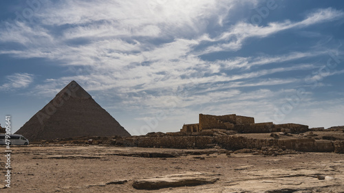 The Great Egyptian pyramid of Chephren against a background of blue sky and clouds. The ruins of an ancient temple are visible nearby. Giza.