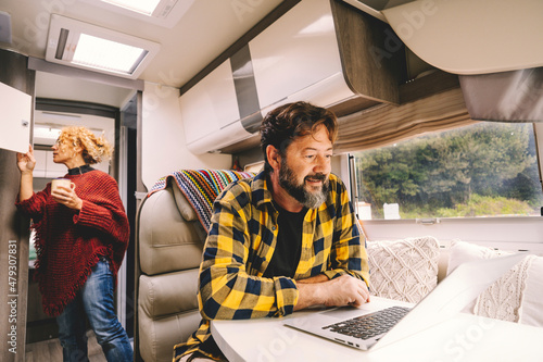 Adult couple travel and enjoy caming car camper van for holiday vacation or vanlife lifestyle - happy man work on laptop on the table and woman looking for stuffs inside the vehicle - nature outdoors