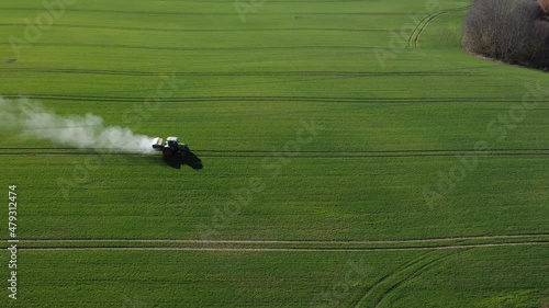 Agriculture tractor spreading fertilizer on  wheat field, aerial view