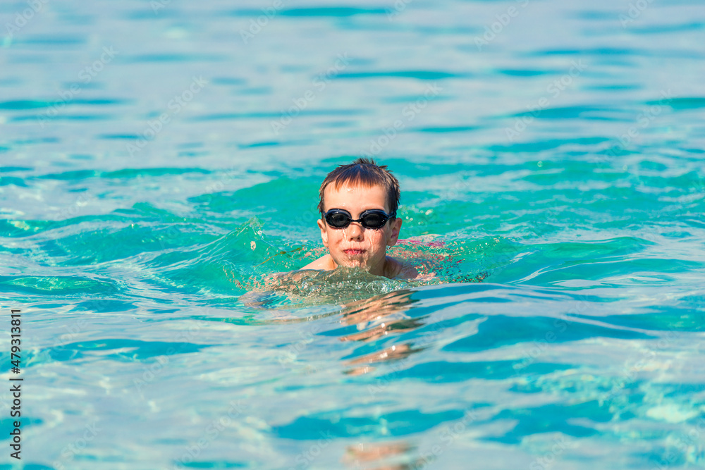 A boy is swimming and having fun in the sea near the shore in swimming goggles