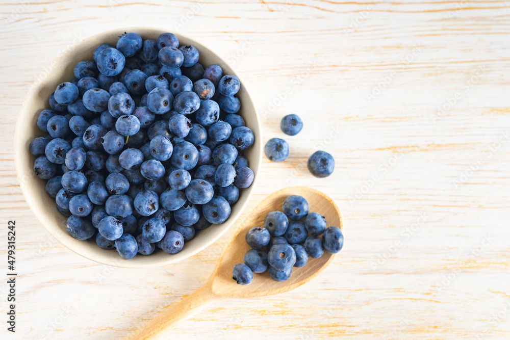 Fresh ripe organic blueberries in bowl and wooden spoon with berries on white wooden background. Flat lay, top view with copy space for text Fresh ripe organic blueberries in bowl and wooden spoon with berries on white wooden background. Flat lay, top view with copy space for text