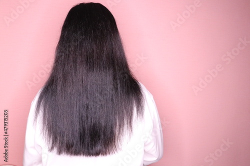 Long dark hair. A woman in a white shirt stands with her back on a light background. 