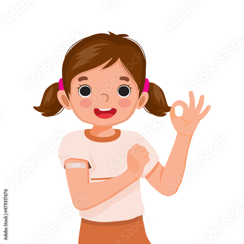 happy little girl showing sticking patch or plaster on her arm after got Vaccine Injection and giving thumb up gestures with smiling facial expression