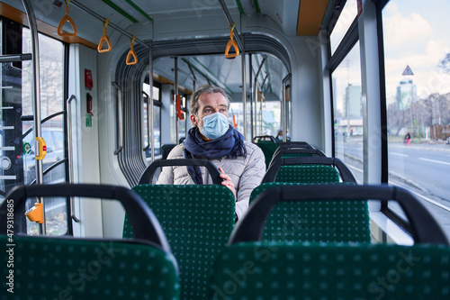 Grey haired man sitting at the transport and keeping protective mask at his face