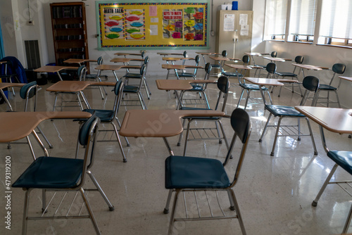 Desks in empty dark high  middle  or elementary school classroom with light coming through windows.