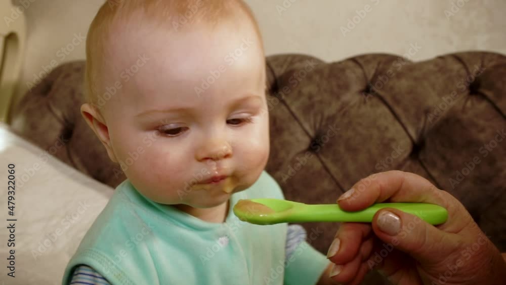 baby sits and grimaces eats from spoon baby sits and grimaces eats from spoon