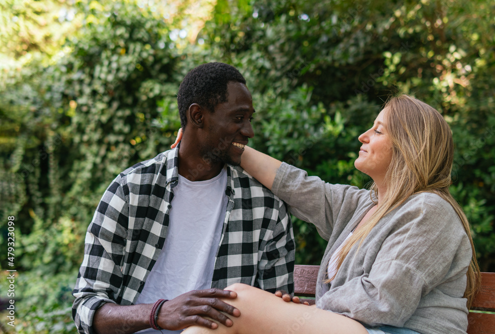 Fototapeta premium A photo of African guy and Caucasian woman having a romantic relationship and comfortable chatting while touching themselves on a park bench.
