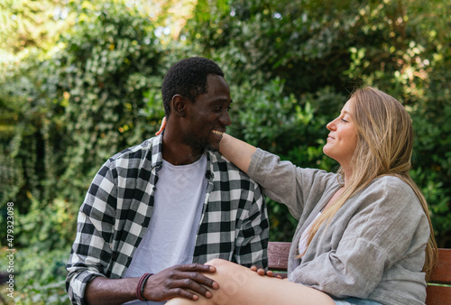 A photo of African guy and Caucasian woman having a romantic relationship and comfortable chatting while touching themselves on a park bench. © anuatmoralesfoto