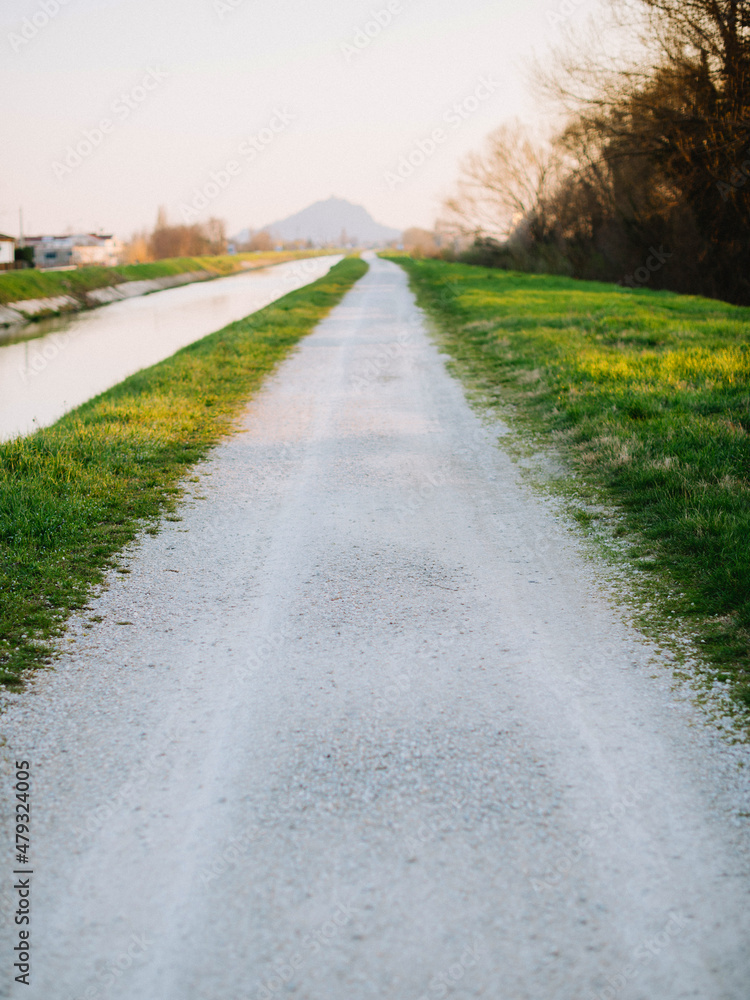white sand road between green grass near river in Italy village white sand road between green grass near river in Italy village