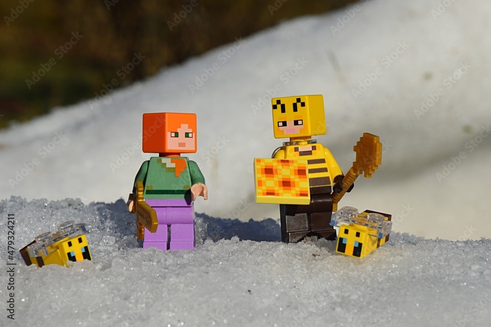 Naklejka premium LEGO Minecraft figures of main character Alex and Beekeeper with honeycomb and golden shovel, surrounded by snow and LEGO bees, winter afternoon sunshine. 