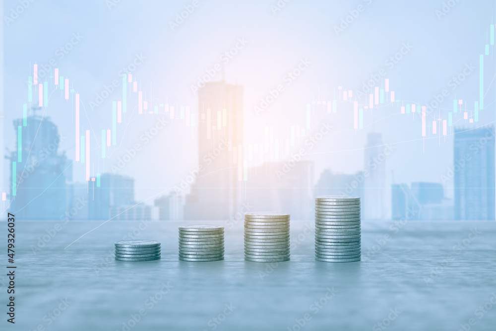 Stack of money coin on office desk with blur background of city building and trading graph. Business and financial concept. 