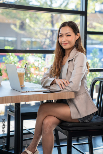Confident of businesswoman wearing suit and looking at camera and smile sitting in the coffee shop with a cup of ice coffee. Shopping online with credit card, freelancer, internet. Business concept