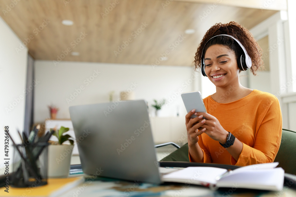 Smiling black woman in wireless headhones using cellphone Smiling black woman in wireless headhones using cellphone