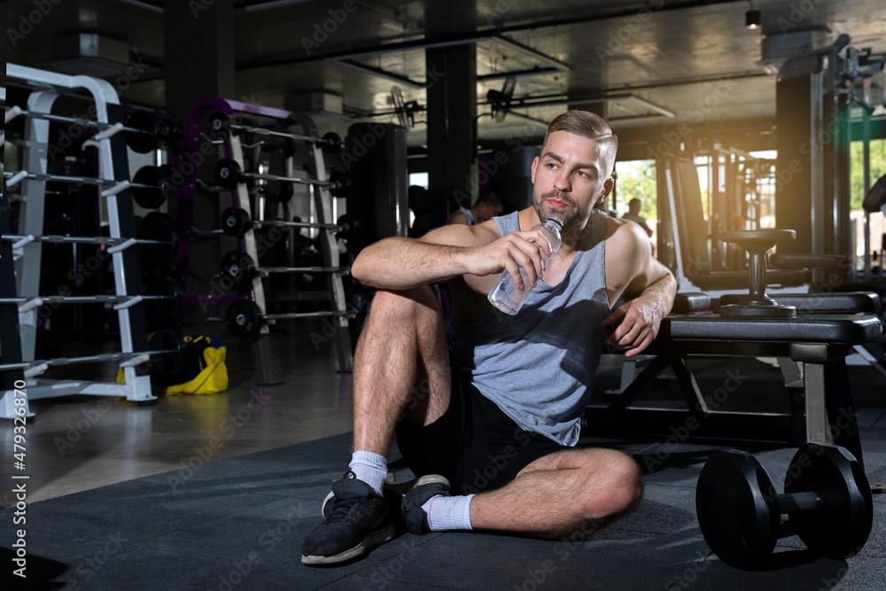 Athletic man relax and drink water after dumbbell work out or exercise in fitness gym. Bodybuilding and healthy lifestyle concept. Athletic man relax and drink water after dumbbell work out or exercise in fitness gym. Bodybuilding and healthy lifestyle concept.