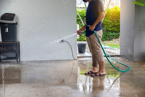 A man Cleaning outdoors  with  Spray water using a hose to the ground