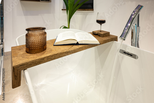 Fotografia Wooden shelf on a freestanding bathtub - soak in the tub and relax with a red wi