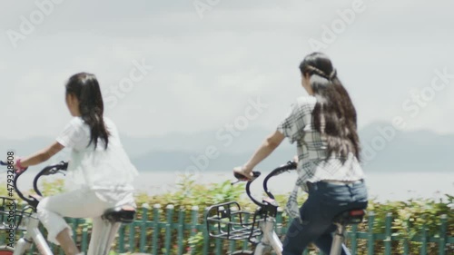 Asian mother and daughter riding bicycles on waterfront promenade in summer