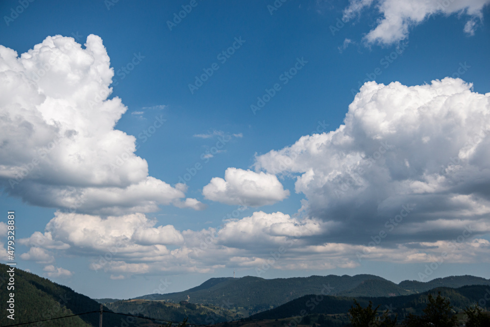 Bright blue sky and thick layer of white fluffy clouds floating above green mountain in Bulgaria.