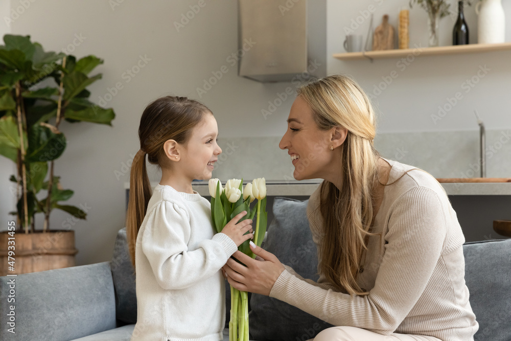 Adorable little daughter girl giving flower bouquet to happy grateful mom. Mum thanking kid for bunch of tulips, celebrating 8 march, mothers day, birthday. Family special event concept Adorable little daughter girl giving flower bouquet to happy grateful mom. Mum thanking kid for bunch of tulips, celebrating 8 march, mothers day, birthday. Family special event concept